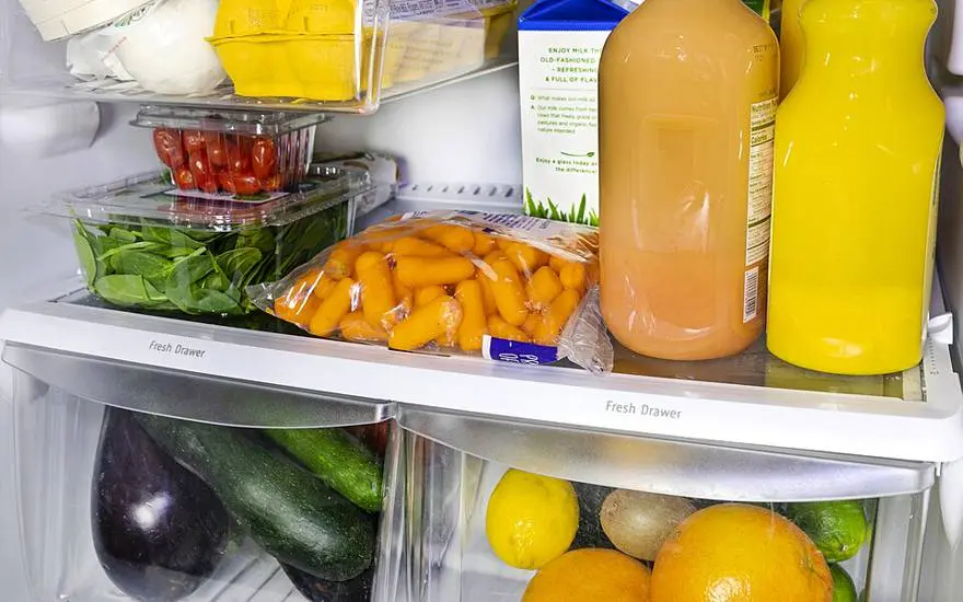An open fridge with eggs, spinach, cherry tomatoes, carrots, aubergine, courgettes and citrus fruit