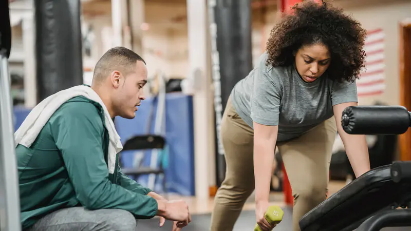 A personal trainer watching a client lift weights in the gym