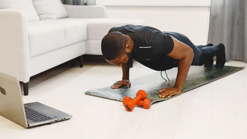 Man doing push-ups at home next to a laptop and dumbbells