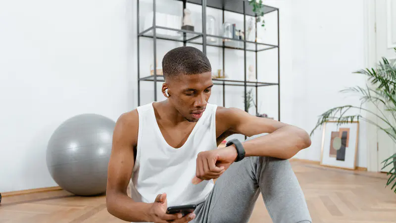A man resting between exercises at home, checking his watch and phone
