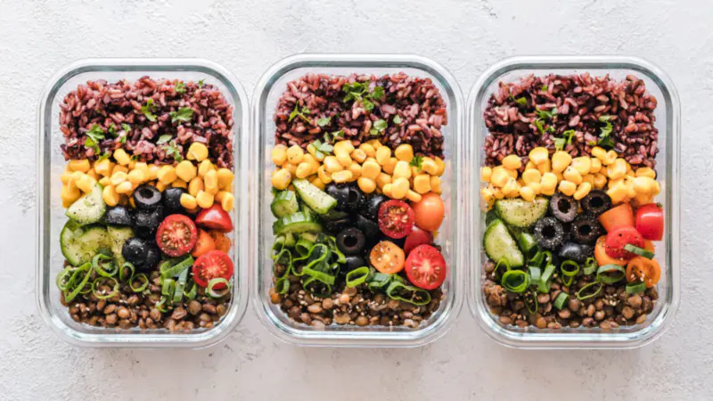 Three meal prep containers filled with grains, beans and vegetables