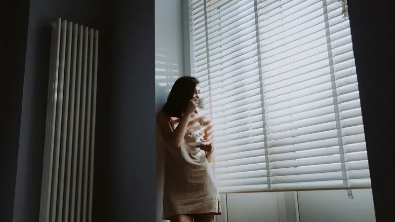 Woman drinking a hot drink by a window in soft morning light