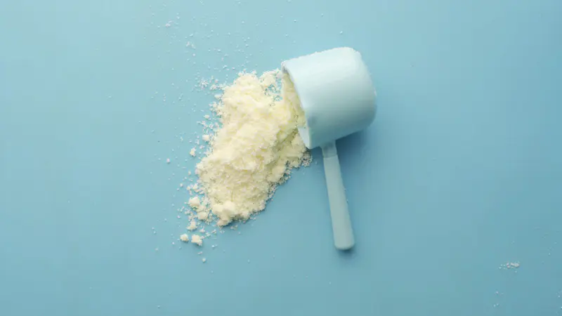Scoop of white supplement powder on a blue background