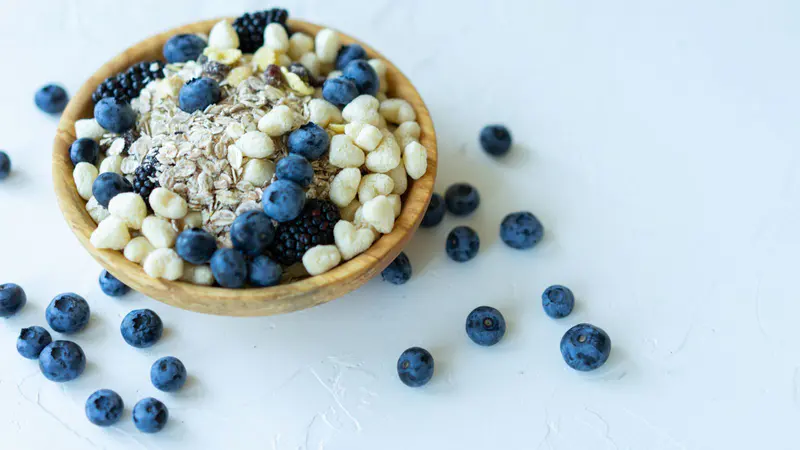 Wooden bowl of oats topped with blueberries and blackberries on a white table