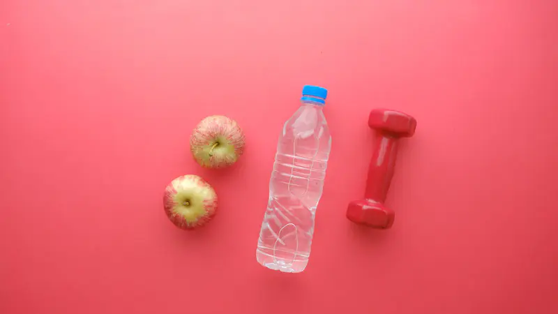 Apples, a bottle of water and a dumbbell on a pink background