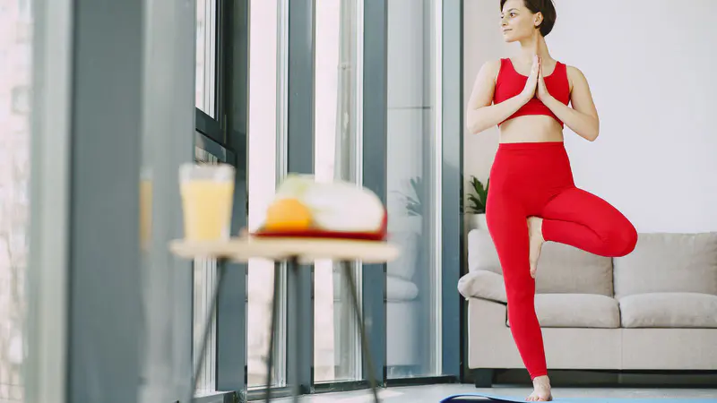 A woman doing a yoga balance pose at home, with a fresh drink nearby