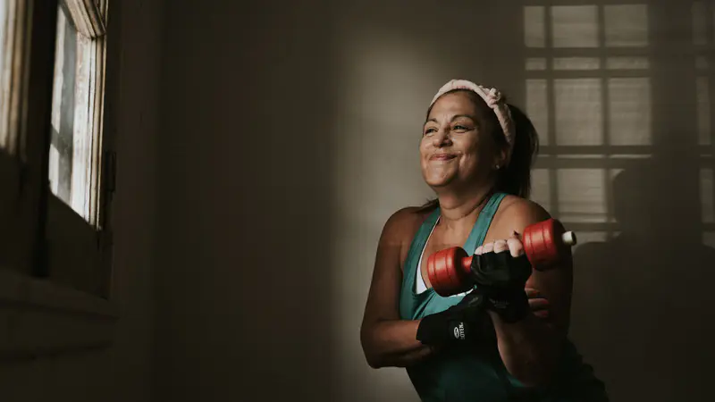 A smiling woman training with dumbbells indoors
