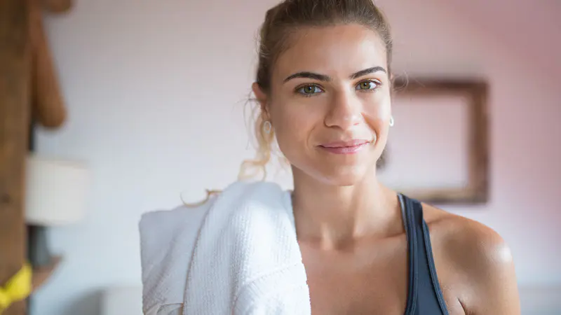A smiling woman with a towel over her shoulders after a workout