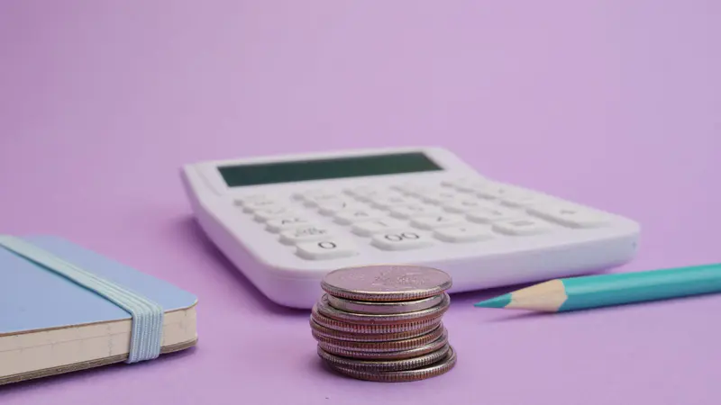 A calculator, a notebook and a stack of coins on a purple background