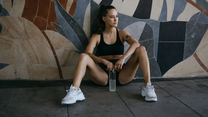 A woman sitting against a wall after a workout, deep in thought