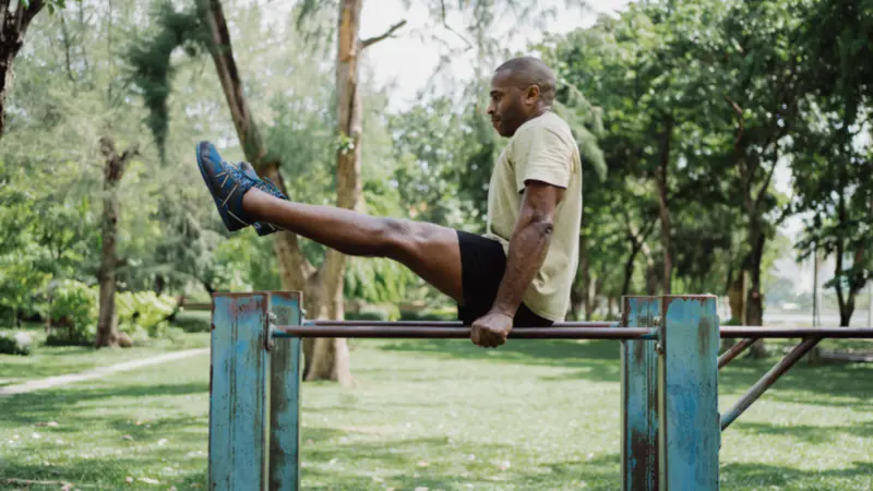 A man doing a bodyweight leg raise on parallel bars in a park