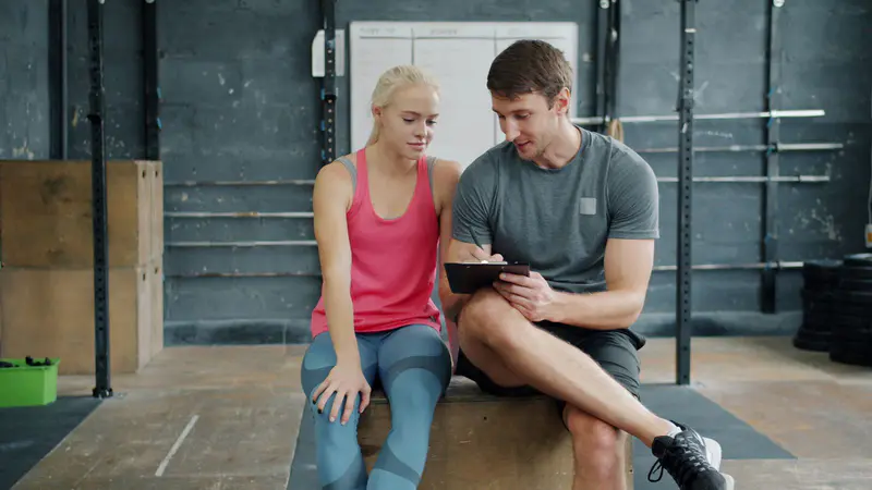 A personal trainer going through a plan on a tablet with a client