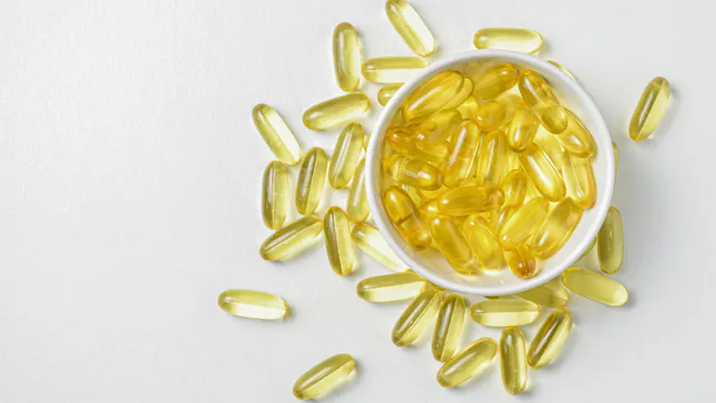 Bowl of golden vitamin D softgel capsules on a white surface