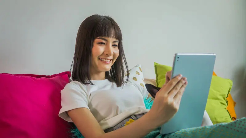 A smiling woman using a tablet on her sofa