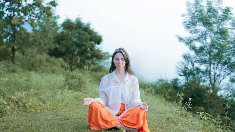 A woman meditating on a grassy hillside