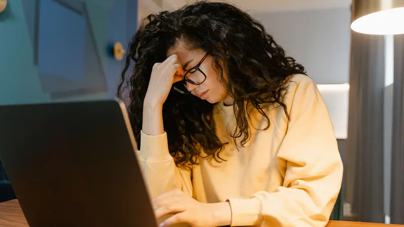 A tired woman resting her head in her hand at her laptop