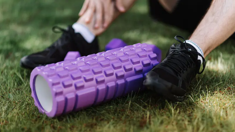 A purple foam roller on the grass beside a pair of trainers